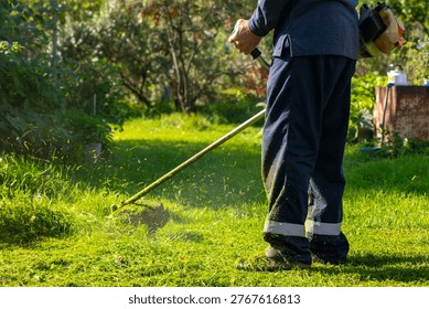 Man using grass trimmer to cut lawn in backyard. Gardener operating string trimmer to maintain greenery. Lawn care equipment, landscaping tool and grass maintenance gardening concept.