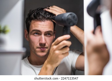 Man using hair dryer while looking himself in the mirror.
