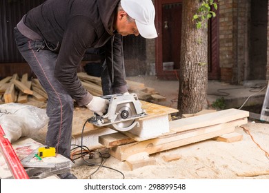 Man Using Hand Held Power Saw to Cut Planks of Wood for Home Construction Leaving Piles of Saw Dust on Floor - Powered by Shutterstock