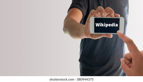 a man using hand holding the smartphone with text wikipedia on display