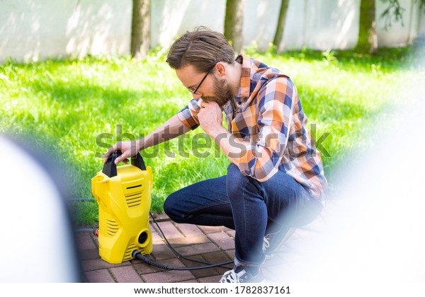 Man using a high pressure washer in the backyard, on\
a sunny day.