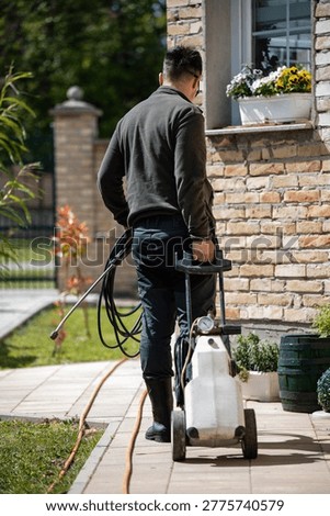 Man using a high-pressure washer to clean outdoor paving stones next to a brick house, performing household maintenance