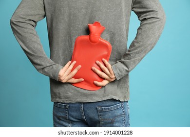 Man Using Hot Water Bottle To Relieve Back Pain On Light Blue Background, Closeup