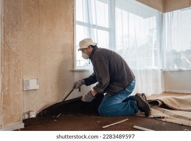 Man using an iron bar to pull up old damaged carpet. Auckland.