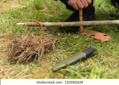 Man using knife and dry materials with friction bow to start a fire in the forest