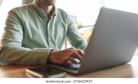 Man using laptop in a cafe while sitting at a wooden table with a smartphone nearby