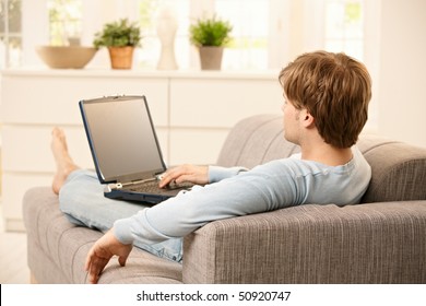 Man Using Laptop Computer Sitting On Couch In Living Room.