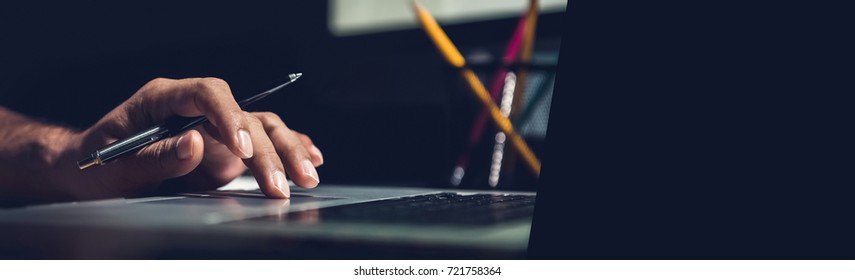 A man using laptop computer working on new project idea at his desk in the office late at night - panoramic web banner with copy space on the right - Shutterstock ID 721758364