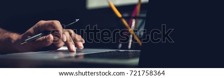 A man using laptop computer working on new project idea at his desk in the office late at night - panoramic web banner with copy space on the right