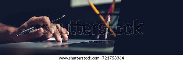 A man using laptop computer working on new project idea at his desk in the office late at night - panoramic web banner with copy space on the right