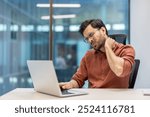 Man using laptop in office shows neck pain and discomfort, representing challenges related to prolonged computer work. Image captures workplace strain and need for ergonomic support during tasks.