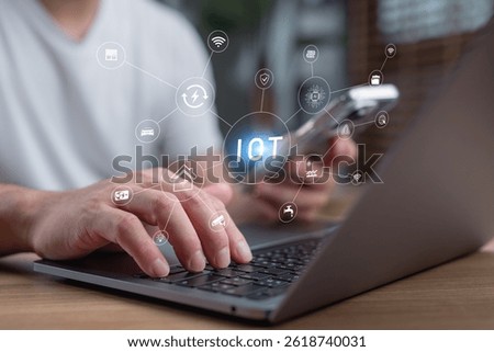 Man using laptop and smartphone with virtual IoT network icons, smart home technology, internet of things connectivity, wireless communication, digital innovation, and intelligent automation systems