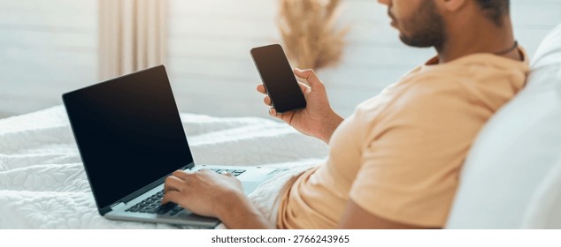 Man Using Laptop and Smartphone While Sitting on Bed in Bright Room During Daytime Hours