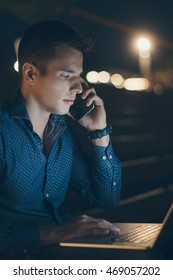 Man Using Laptop And Talking On The Mobile Phone At The Night