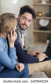 man using laptop while his girlfriend makes call on smartphone