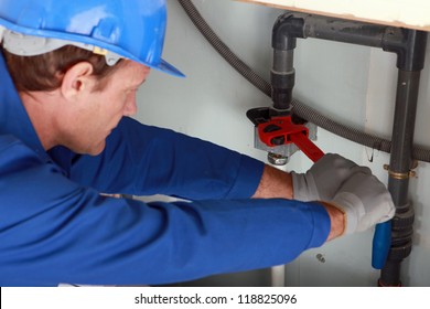 Man Using A Large Red Wrench On Some Interior Water Pipes