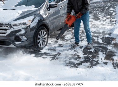 A man using a leaf blower to clear light powdery snow from car and the driveway