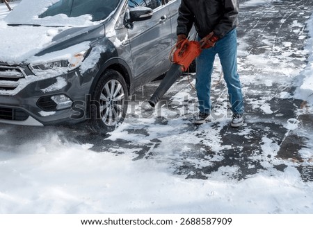 A man using a leaf blower to clear light powdery snow from car and the driveway