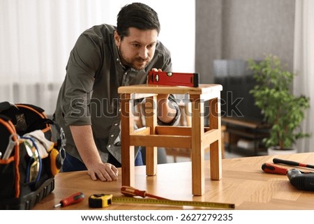 Man using level tool while repairing wooden stool at home