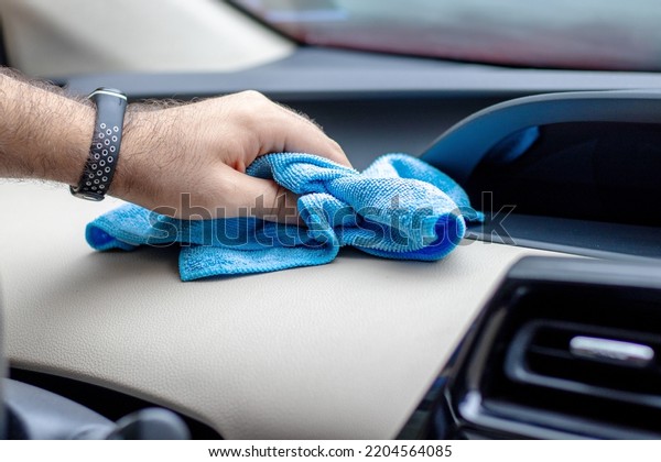 man using microfiber cloth and spray for\
interior car cleaning.unrecognizable man hand with fitness bands\
tracker on hand beige light surface.car wash business.dirty dusty\
inside auto,wipe own\
vehicle