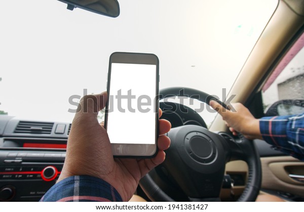 Man Using Mobile Phone\
Device While Driving. Cropped shot view Man looking smart phone in\
a car.