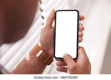 Man using mobile phone with empty screen near window indoors, closeup