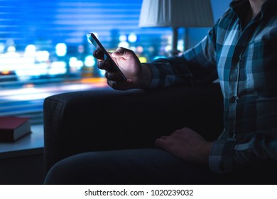 Man Using Mobile Phone Home Late At Night. Guy Looking Messages With Modern Cellphone In Dark. Unfaithful Husband Cheating And Texting With Another Woman. Secret Or Illegal Business. Sitting On Couch.