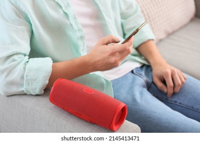 Man Using Mobile Phone On Sofa With Modern Wireless Portable Speaker, Closeup