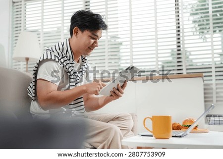 Man are using a mobile phone playing social media and laptop wifi connection sitting on sofa, home office workplace lifestyle people.