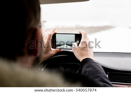 Man using mobile phone. Taking photo. Horizontal mock up. Shot with third-person view in the car in winter in the countryside road
