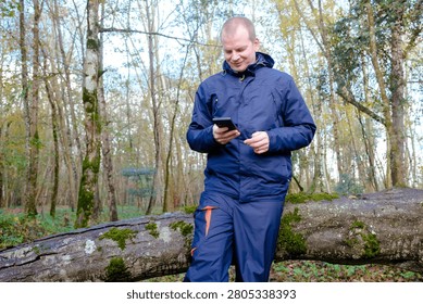 Man using a mobile phone while standing by a fallen log in a woodland