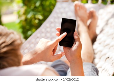 Man using mobile smart phone while relaxing in a hammock - Powered by Shutterstock