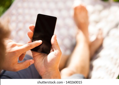 Man using mobile smart phone while relaxing in a hammock - Powered by Shutterstock