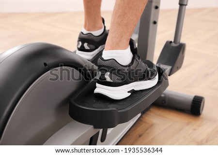 Man using modern elliptical machine indoors, closeup