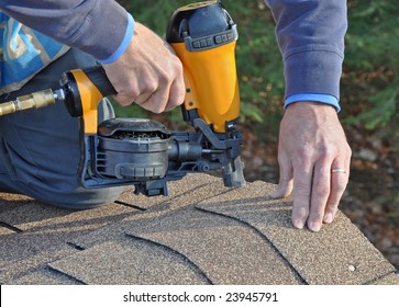 Man Using Nail Gun To Attach Asphalt Shingles To Roof