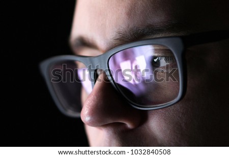 Man using online dating application with smartphone or watching a picture of a young woman. Video phone call. Long distance relationship. Stalker watching photos. Reflection of screen on glasses.