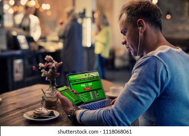 Man using online sports betting services on phone and laptop - Shutterstock ID 1118068061