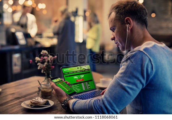 Man using online sports betting services on phone\
and laptop