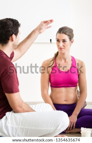 Man using pendulum for hypnotizing the fit young woman