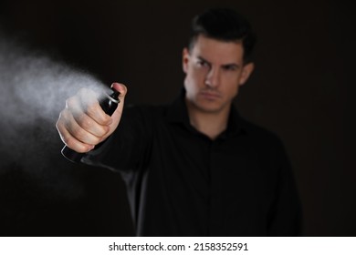 Man using pepper spray against black background, focus on hand