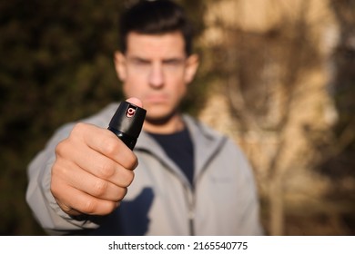 Man using pepper spray outdoors, focus on hand. Space for text