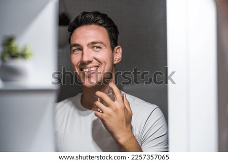 Man using perfume while looking himself in the mirror.