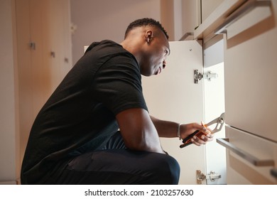 Man Using Pliers To Repair Cupboard Drawer In Kitchen