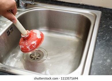 Man using a plunger with one hand and  water in sink, used to clean a clogged / blocked kitchen sink