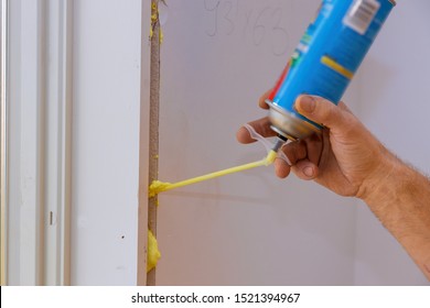 Man using polyurethane foam for installing a window on a handsome worker in action during the installation