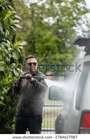 Man using a power washer cleaning an automobile in the driveway, performing car detailing and washing a vehicle
