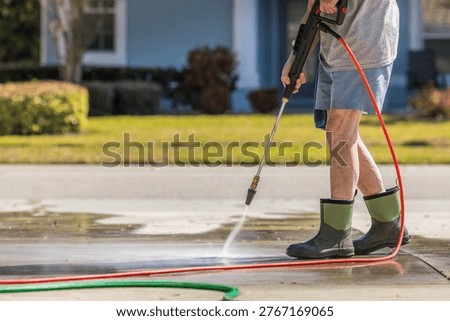 Man using pressure washer to power wash residential concrete driveway sidewalk.