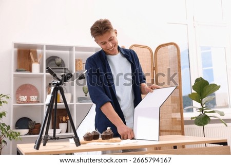 Man using reflector to take picture of chocolate muffins in studio. Professional food photography