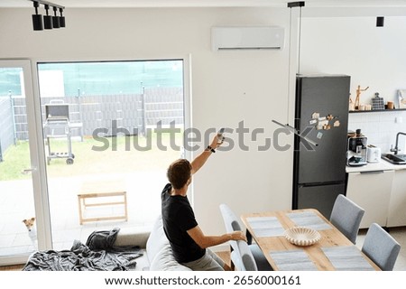 Man using remote control to adjust air conditioner in bright modern living room. Person adjusting temperature for cooling during hot summer days. Concept of home comfort