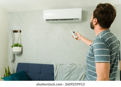 Hombre que usa un control remoto, ajustando la temperatura de su unidad de aire acondicionado mini-split durante un caluroso día de verano